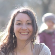 Porträt von Anne Hackenberg lächelnd in der Natur, im Hintergrund ist verschwommen ein Kind zu sehen