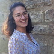 Porträtfoto von Danijela Klich – sie steht lächelnd vor einer Steinmauer, von der Sonne beschienen