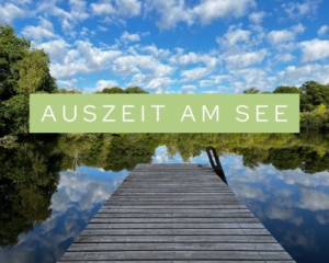 Foto eines spiegelglatten Sees, in dem sich die Wolken spiegeln. Schriftzug. Auszeit am See