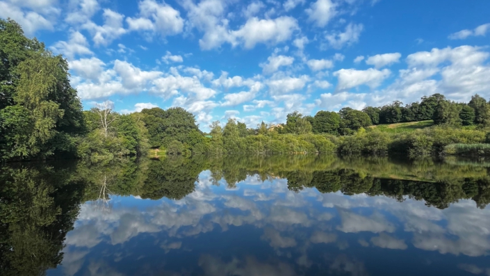 Foto: Himmel mit Wolken spiegelt sich in einem See.