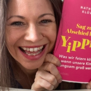 Foto von Nathalie Klüver, wie sie lachend ihr neues Buch "Sag zum Abschied leise Yipiieh" in die Kamera hält.