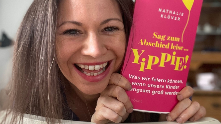 Foto von Nathalie Klüver, wie sie lachend ihr neues Buch "Sag zum Abschied leise Yipiieh" in die Kamera hält.