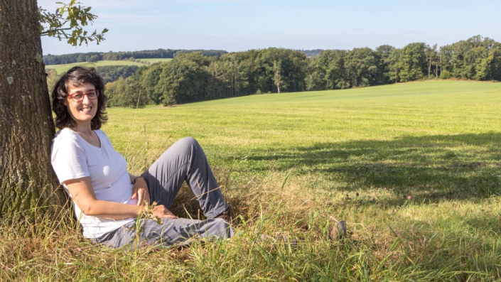 Sandra Knümann sitzt auf einem Feld, mit dem Rücken an einen Baum gelehnt