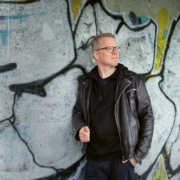 Foto: Der Autor und Comic-Zeichner Flix lehnt an eine Wand, die mit Graffiti bedeckt ist.