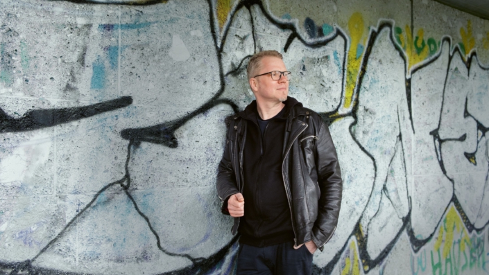 Foto: Der Autor und Comic-Zeichner Flix lehnt an eine Wand, die mit Graffiti bedeckt ist.