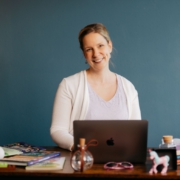 Foto von Diana Wegel, lächelnd am Schreibtisch mit Laptop und Lernutensilien