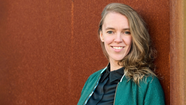 Foto von Stefanie Bohle, lehnt an einer Wand und lächelt in die Kamera