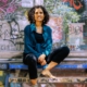 Foto von Kiran Deuretzbacher, sitzend vor einer Graffiti-Wand