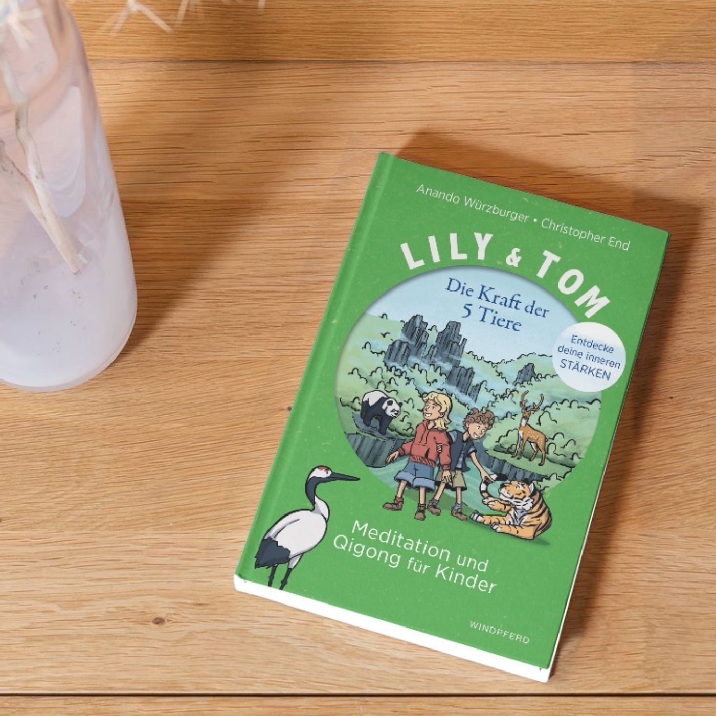 Das Buch "Lily & Tom: Die Kraft der 5 Tiere" liegt auf einem Holztisch.