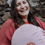 Porträtfoto von Ramona Noll, die ein große Kissen in Brustform vor sic hält und lacht